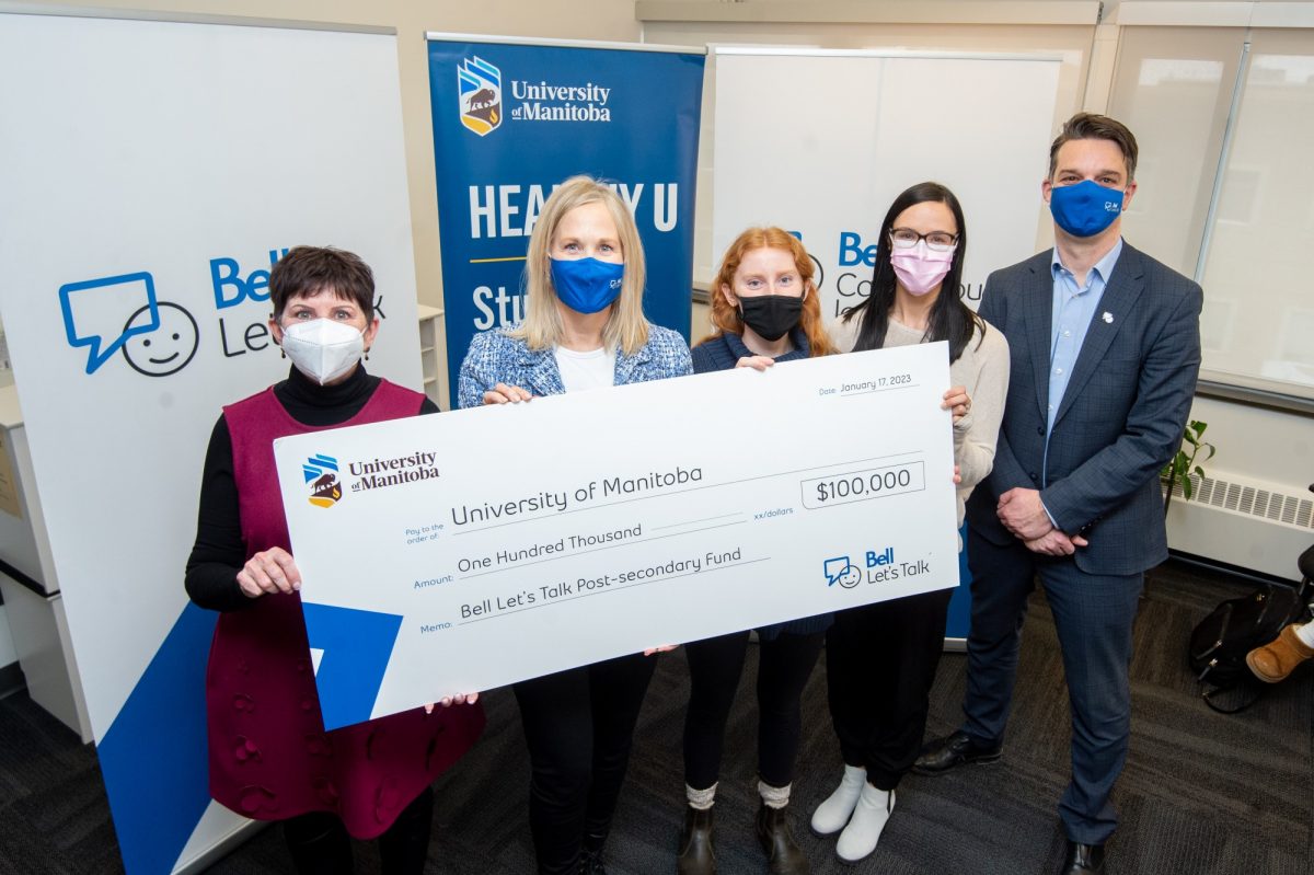 Representatives from UM and Bell Let's Talk hold a large cheque for $100,000