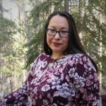 Janine Windolph in flowered blouse in front of a forest of pine trees.