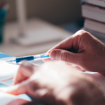 Person reading textbook with pen in hand