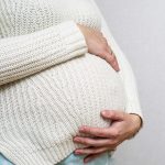 A pregnant woman holds her hands on her belly.