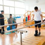 Young men exercising in the physical therapy room next to their health care providers.