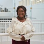 Carine Bado is in a white shirt standing next to a white railing.