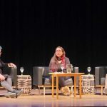 Three women sitting on armchairs on a stage.