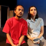 Brother and sister sitting shoulder to shoulder listening to a walkman through headphones.