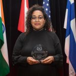 Judy Jayasuriya Standing with a Trophy in front of a set of five flags
