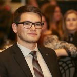 Man with glasses and tie sits at a table at an event