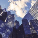 Looking up at tall office buildings in a downtown scene with clouds in a blue sky.