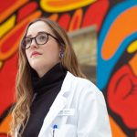 Maizy North looks away in front of Indigenous mural.