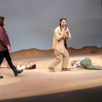 Four student actors on a barren stage. Two actors lying down, one standing and one crouching.