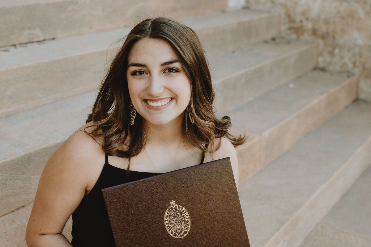 Woman smiling holding her diploma on staircase.