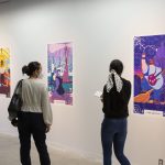 People walking past and viewing colourful artwork in an exhibition space.