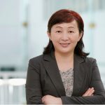 Lady standing with arms crossed in suit jacket.