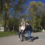 3 students walk across campus in the sunshine.