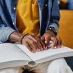 Closeup of a university student with a visual impairment reading a braille book.