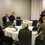 Four people sit at a round table. Drs. François and Jacobsen sit at another round table. Dr. Doupe stands at a lectern.