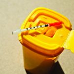 A syringe sits atop a medical waste container inside a hospital.