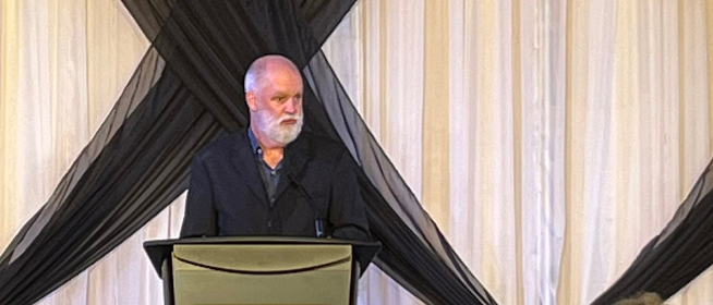 Portrait of André Picard, standing at a podium.