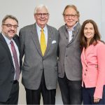 three men and one woman pose in business attire pose for a photo