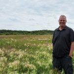 man stands in a field smiling