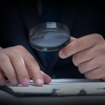 Photo of hands using a magnifying glass over paper.
