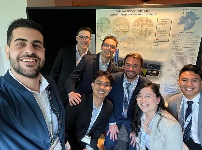 A group of students smiling in front of their capstone project poster