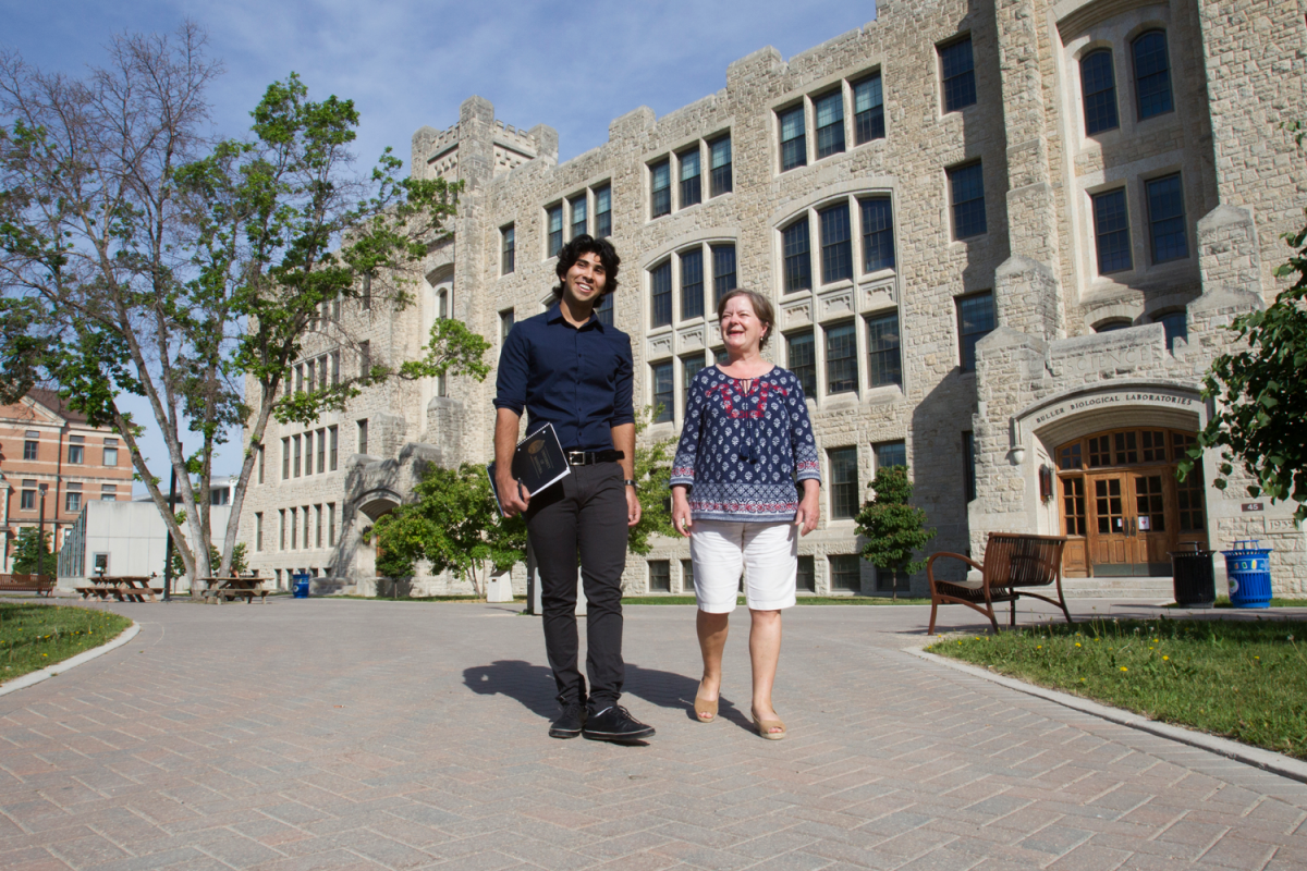 Work-study student and staff walking infront of the castle like buller building on the UM Fort Garry Campus