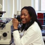 Dr. Yvonne Myal sits in front of a microscope in her lab.