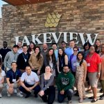 A big group of U M students standing in front of the Hecla Lakeview hotel sign in Manitoba.