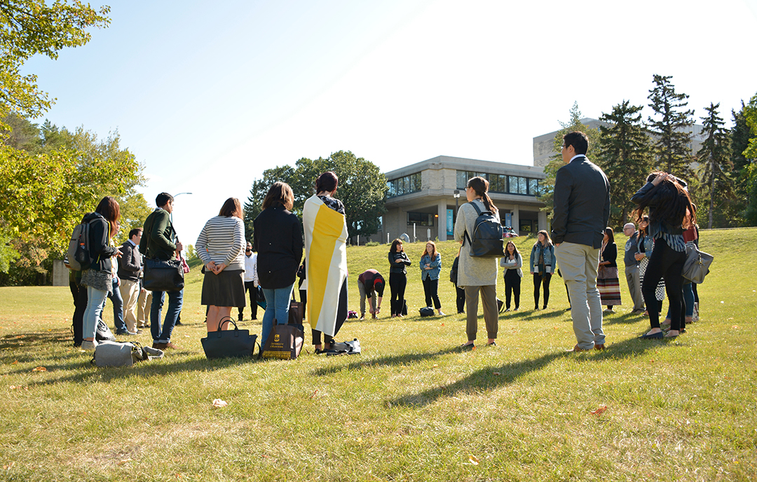 Law Students stand in a circle in a field with the faculty of law building on a hill in the distance