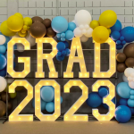marquee letters spelling "grad 2023" surrounded by white, brown, gold and blue balloons