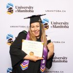 asper graduate stands in celebratory pose in graduation cap and gown with degree