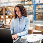 Woman looking busy working on laptop at a distribution warehouse.