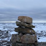 View of an Inukshuk with snowy, rocky landscape.