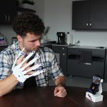Male student wearing a plastic glove and looking at a smartphone.