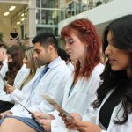 About 10 students wearing white coats read the Pledge of Professionalism off of the programs they are holding.