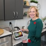 Jacquie Ripat stands at a kitchen counter, operating a touchscreen computer.