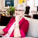 Senator Patricia Bovey in wearing a pink/red sweater siting in a chair smiling toward the camera.
