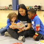 A childminder reads a book to two kids.