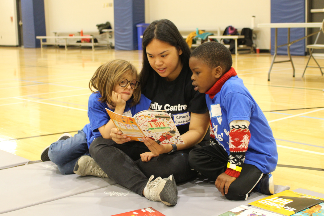 A childminder reads a book to two kids.