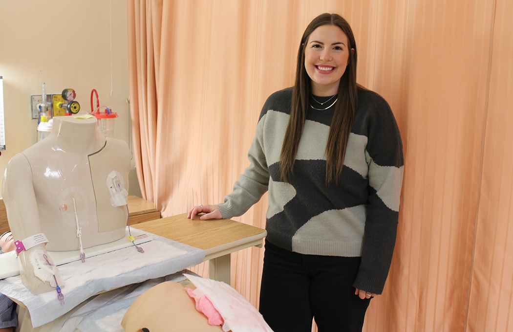 A nursing student posing at a simulation lab bedside.