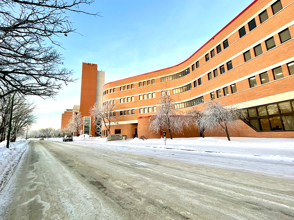 Frosty morning outside the Drake Building. The sky is a light blue, no leaves on trees, the rust building has frost covered trees.