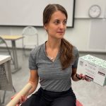 A young woman sits on a large red ball, holding a tissue box and a paper towel roll.