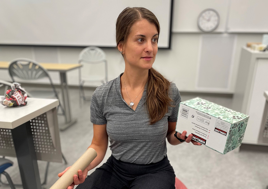 A young woman sits on a large red ball, holding a tissue box and a paper towel roll.