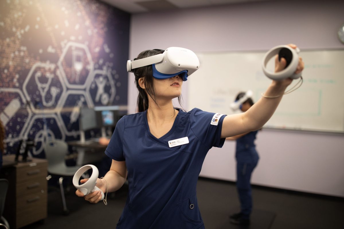 A nursing student wears a virtual reality headset and holds virtual reality hand controllers.