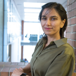 Azadeh Tabiban smiling and leaning against a brick window.