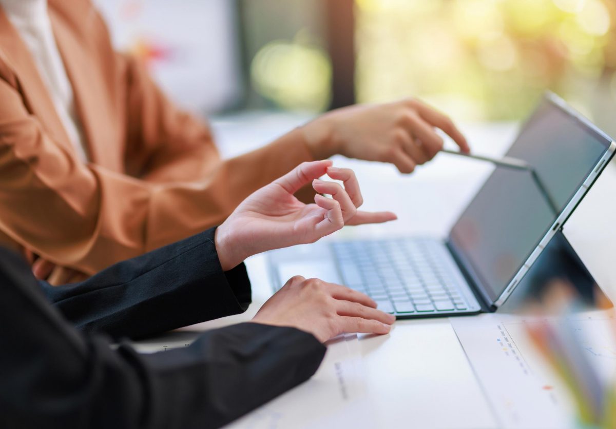 Two people working at a laptop with a woman pointing something out on the screen.