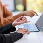 Two people working at a laptop with a woman pointing something out on the screen.