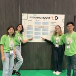 Jessica Marinelli and Camille Prefontaine wearing bright green shirts in the left, with one pointing to the poster behind them, Oleksandra Havruk and Louis Cheng on the right wearing bright green shirts with one pointing to the poster behind them. The poster is on a wall with dark wooden panels.