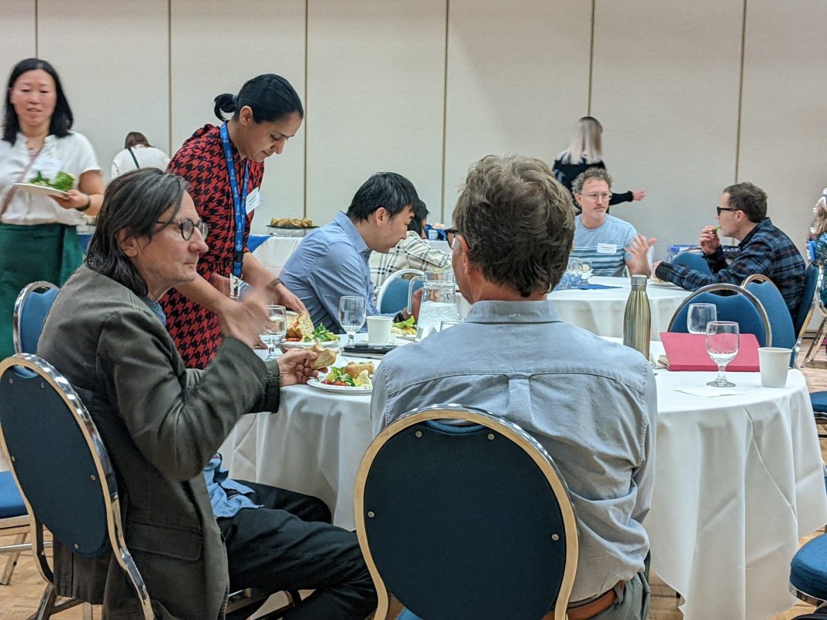 People sitting around tables at a venue eating and talking to each other.