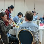 People sitting around tables at a venue eating and talking to each other.